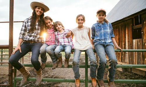 Mary Heffernan and her four daughters sitting on a green gate next to their barn at Five Marys Farms